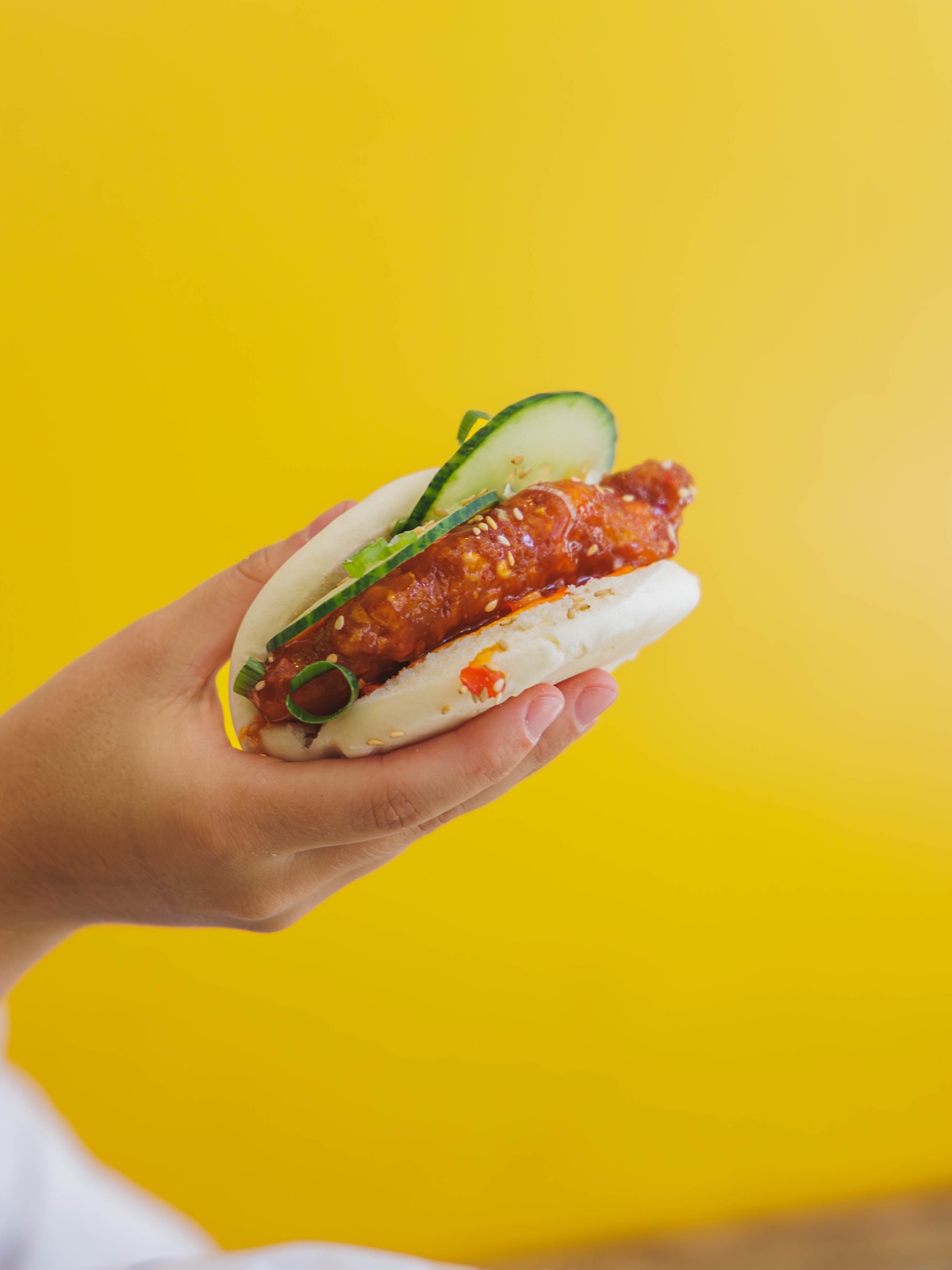 Chikin Bao Chungchun garni de poulet croustillant et concombre, sur fond jaune vif