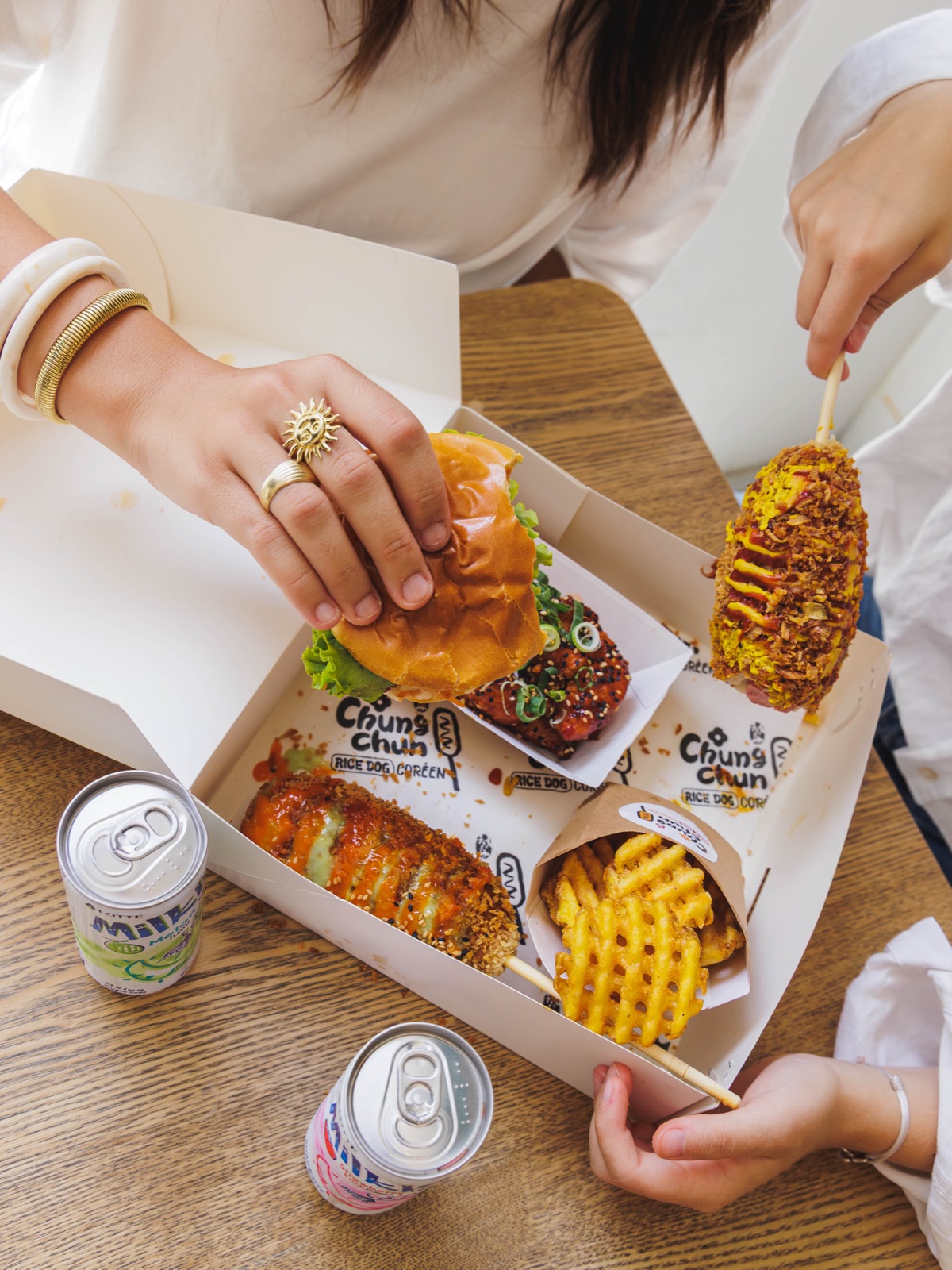 Amies partageant Rice Dogs, burger et frites autour d'une box Chungchun