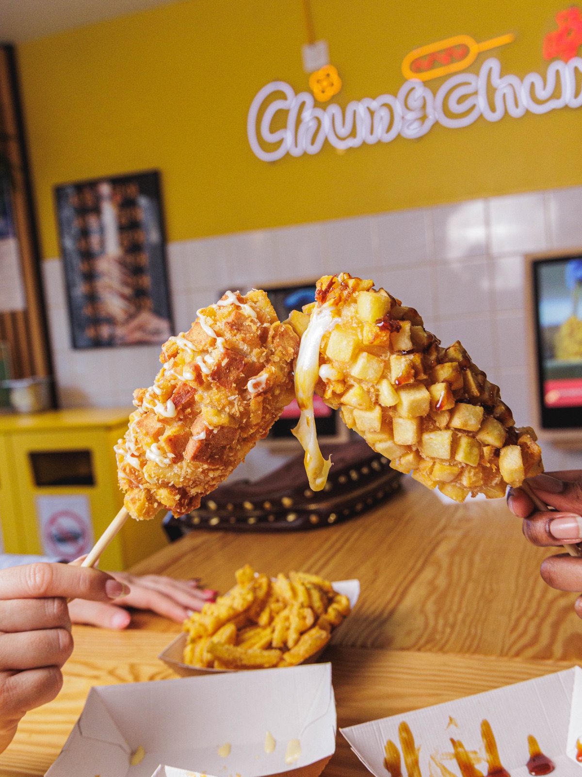 Deux clients trinquant leurs Rice Dogs croustillants au-dessus de waffle fries, en salle Chungchun